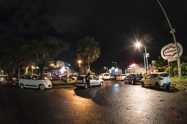 Un estacionamiento nocturno con varios coches y una persona caminando.