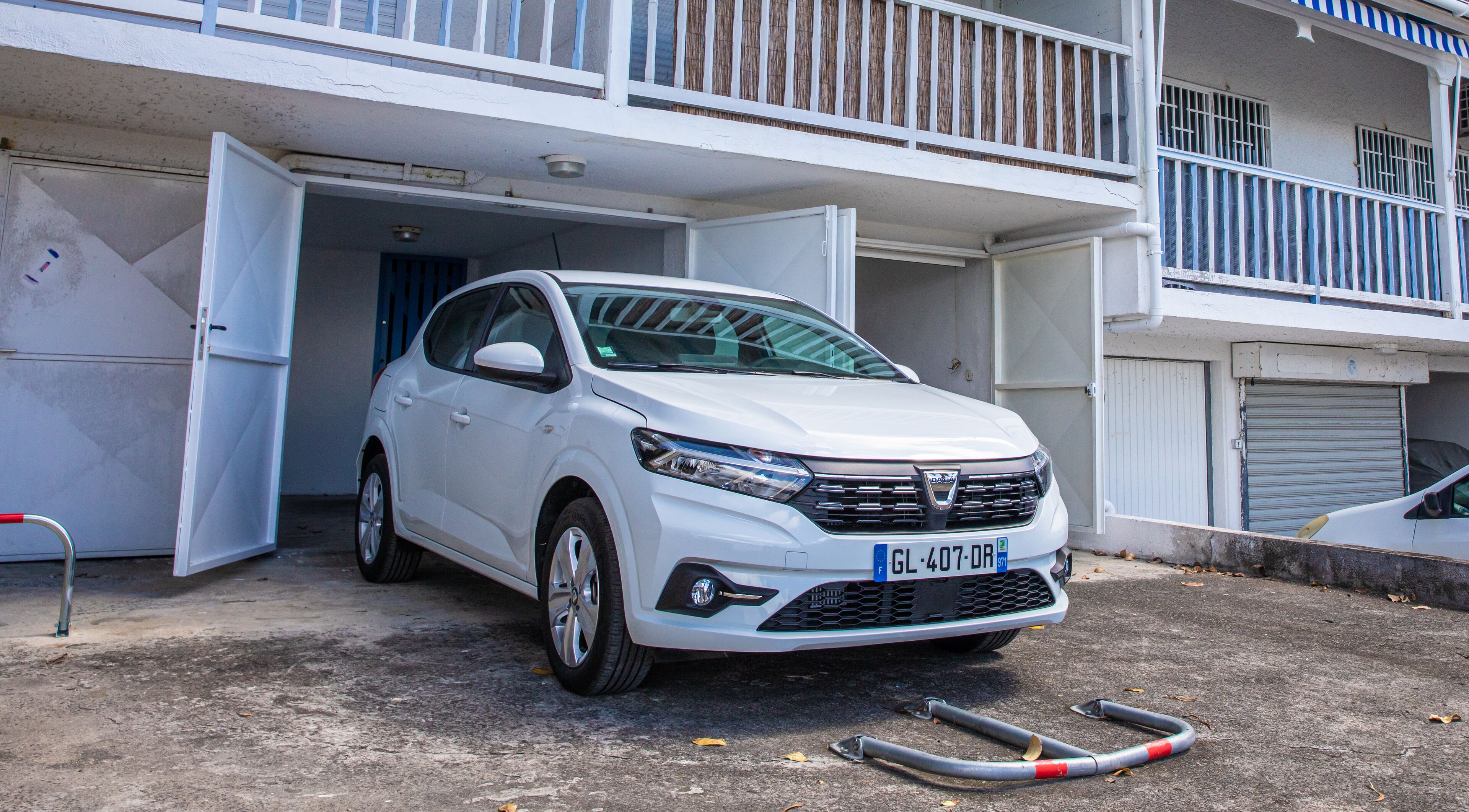 A white car parked in front of a building with a balcony.
