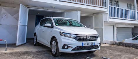 A white car parked in front of a building with a balcony.