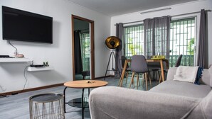 A modern living room with a flat-screen TV, a dining table with chairs, a sofa, and a floor lamp.