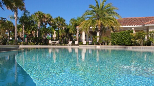 A clear swimming pool with lounge chairs and palm trees. - Lakefront with Resort Amenities, 10 Mins from Disney (Kissimmee)