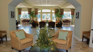 A spacious lobby with wicker furniture, a central plant, and large windows offering a view of the outdoors. - Lakefront with Resort Amenities, 10 Mins from Disney (Kissimmee)