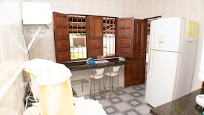 A kitchen with wooden cabinets, a refrigerator, and two bar stools. - HOUSE ON FRENCH BEACH (Praia do Francês)