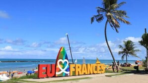 A beach with a large sign reading "EU & FRANCE" and a colorful sailboat. - HOUSE ON FRENCH BEACH (Praia do Francês)
