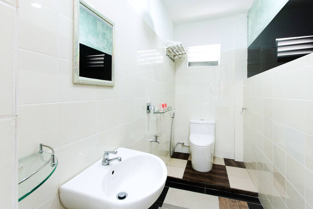 Un bany modern amb rajoles blanques, un lavabo de vidre, un vàter i una dutxa.
