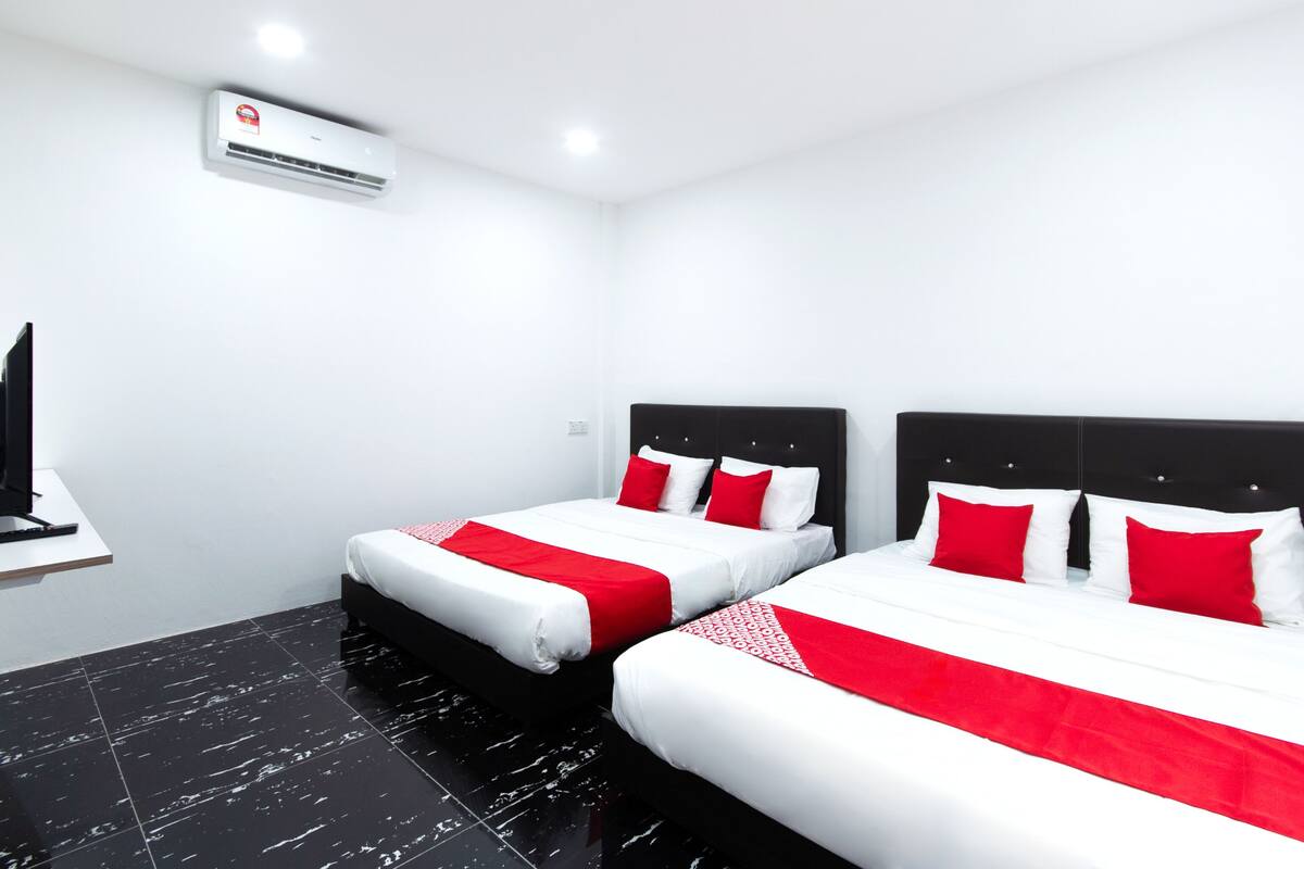 Una habitació d'hotel amb dos llits, cadascun amb roba de llit blanca i vermella, un panell de fons negre i aire condicionat fixat a la paret.