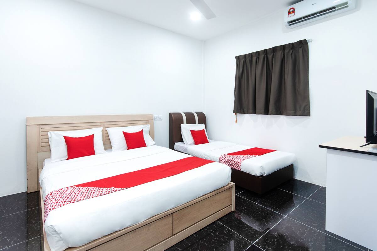 Habitació d'hotel amb dos llits, un ventilador de sostre, aire condicionat, una taula amb un ordinador i una finestra amb cortines.