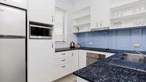 A modern kitchen with white cabinets, a black countertop, a built-in microwave, and a dishwasher. - 3 Bedroom Poolside Villa (Sunshine Coast)