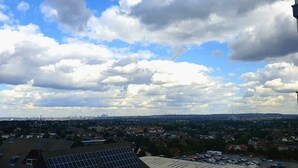 A cityscape with a view of a large building with solar panels on the roof, a parking lot, and a cloudy sky. - New Modern Penthouse apartment with a fantastic view (Sutton)