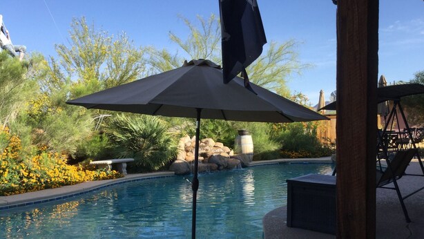 Ein Pool mit Pergola und Sonnenschirm, umgeben von angelegten Gärten und einem Steinelement.