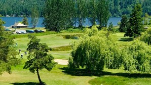 Ein Golfplatz mit einem See und bewaldeten Hügeln im Hintergrund.