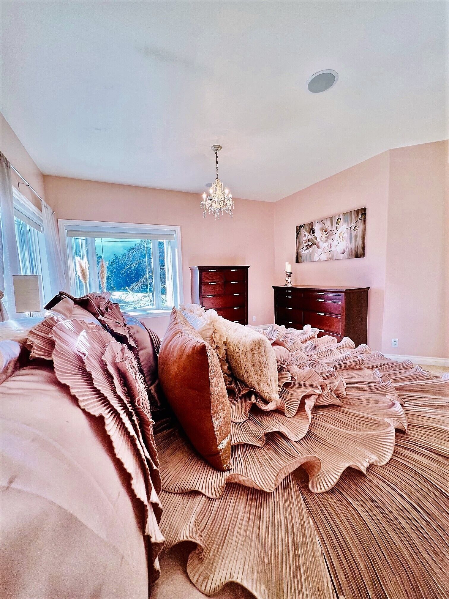 A bedroom with a large bed, a chandelier, a fireplace, and a window with a view of trees.