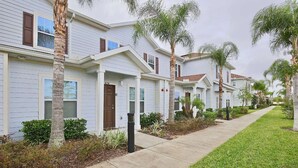 A row of single-story houses with a uniform architectural style, featuring front porches and palm trees. - Lovely Townhouse in a resort located less than 10 minutes from Disney complex. (Kissimmee)