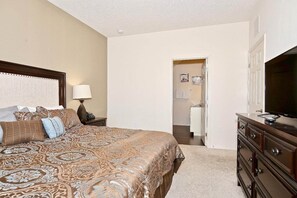 A bedroom with a large bed, a dresser, a television, and a bathroom visible through an open door. - Lovely Townhouse in a resort located less than 10 minutes from Disney complex. (Kissimmee)