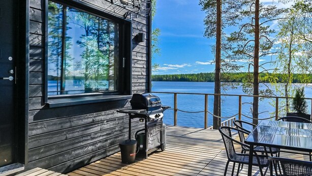 A wooden deck with a grill and chairs, overlooking a lake.