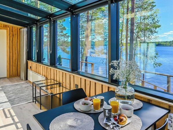 Ein Essbereich mit gedecktem Tisch für ein Frühstück mit Blick auf einen See und Bäume.