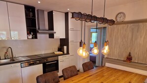 A modern kitchen with a wooden dining table, built-in appliances, and pendant lighting. - Comfortable vacation home near ski slopes, large sunny garden  (Leogang)