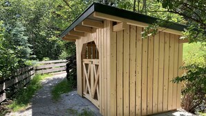 A wooden shed with a sloped roof, located beside a gravel path with a wooden fence. - Comfortable vacation home near ski slopes, large sunny garden  (Leogang)