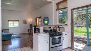 Een moderne keuken met een ingebouwde kookplaat, oven en koffiezetapparaat. Er is een zithoek met een blauwe bank en een raam met uitzicht op de omgeving.