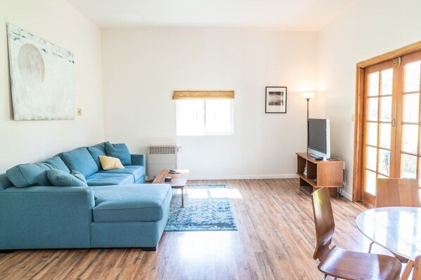 A living room with a blue sofa, a coffee table, a TV stand, and a dining table with chairs.