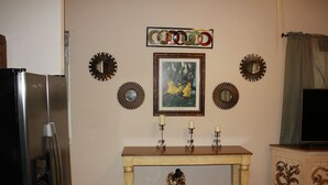 A dining area with a wooden table, a framed picture, decorative mirrors, and a fruit bowl.