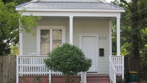 A single-story house with a white front porch, a mailbox, and a small tree in front.