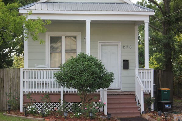 A single-story house with a white front porch, a mailbox, and a small tree in front.