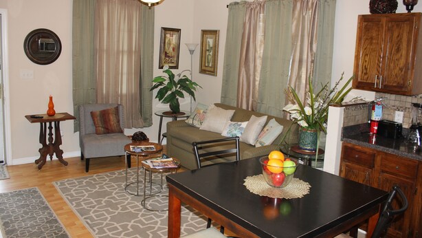 A living room with a dining table, sofa, and a kitchen area with cabinets and appliances.