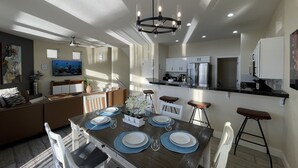Une cuisine moderne avec des meubles blancs, un réfrigérateur en acier inoxydable et un coin repas doté d’une table en bois, mise pour quatre personnes.