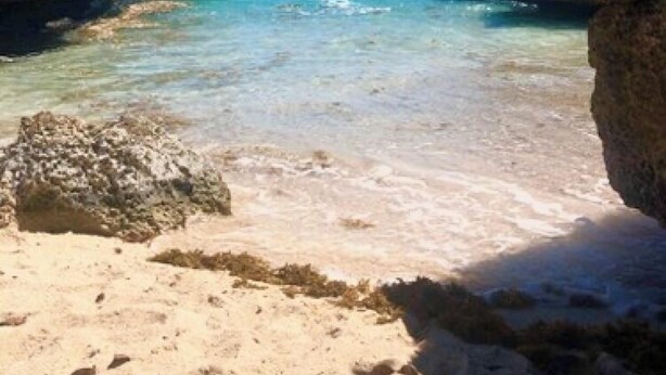 Uma praia com águas turquesa cristalinas, falésias rochosas e uma faixa de areia.