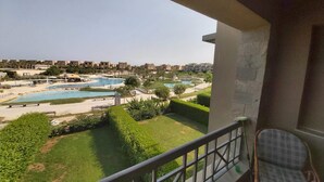 En balkon med udsigt over et poolområde, inklusive flere pools og en velholdt græsplæne.