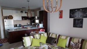 En moderne stue med sofa og sofabord, et køkkenområde med spisebord, og en lysekrone.