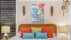 Ein Bett mit bunten Kissen, eine Wand mit einem Hawaii-Plakat und zwei Nachttische aus Holz mit Lampen.