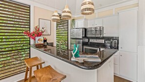 Eine moderne Küche mit weißen Schränken, einer Granit Arbeitsplatte und einer zentralen Kücheninsel. Man sieht drei Pendelleuchten, einen Kühlschrank und eine Mikrowelle.