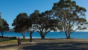 Een buitenbasketbalveld met een net, omringd door bomen en met uitzicht op een waterpartij.