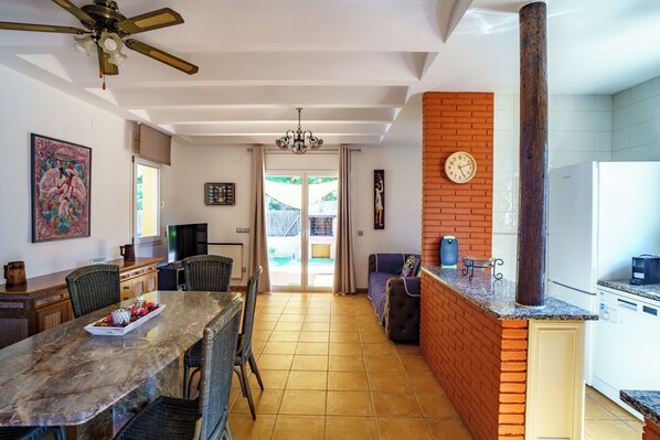 A spacious kitchen with a brick accent wall, a dining area with a marble table, and a ceiling fan.