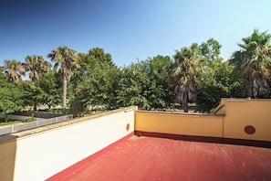 A rooftop terrace with a red floor, surrounded by trees and a clear sky.
