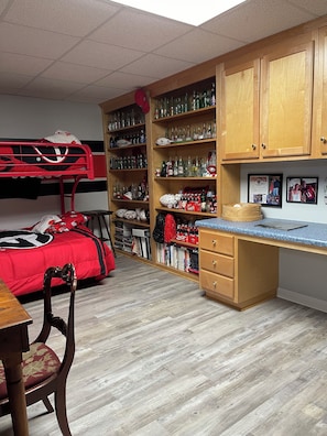 A dormitory room with bunk beds, a desk, shelves with various items, and a wooden cabinet.