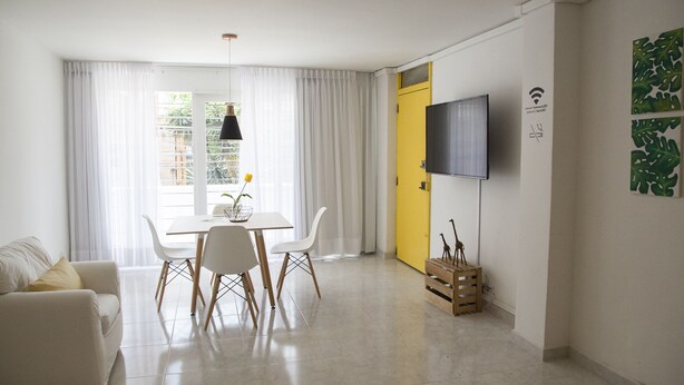 Een moderne woonkamer met een eethoek, een gele deur en een tv aan de muur.