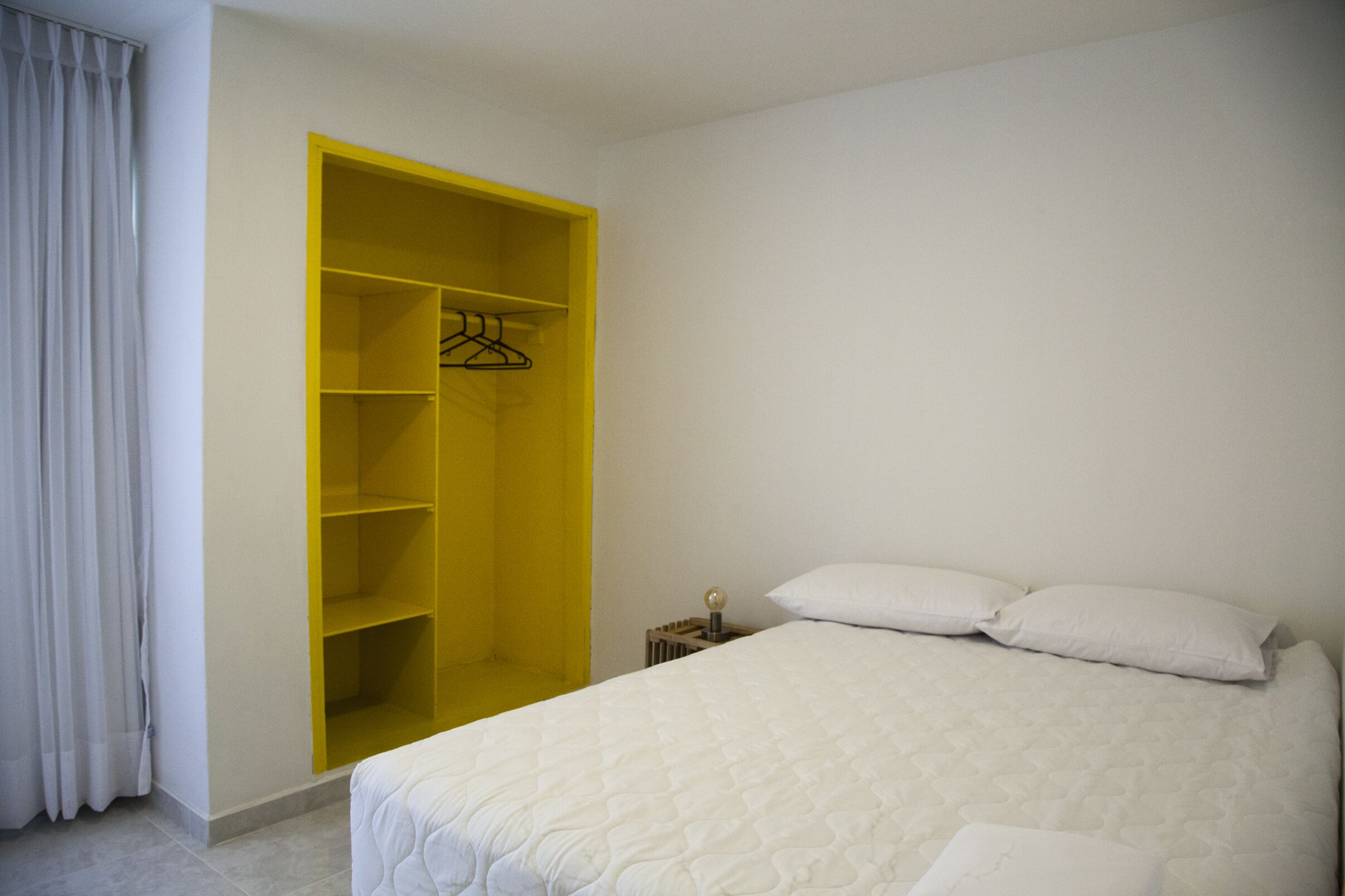 A bedroom with a large yellow wardrobe, a bed with white bedding, and a nightstand with a lamp.