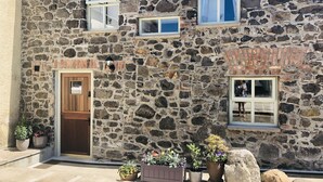 A stone building with a wooden door, multiple windows, and potted plants. - 5 Star Coachmans cottage. Built in the mid 18th Century. (Stranocum)