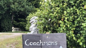 A sign for Coachman's Cottage with an arrow pointing upwards, surrounded by greenery and a statue. - 5 Star Coachmans cottage. Built in the mid 18th Century. (Stranocum)