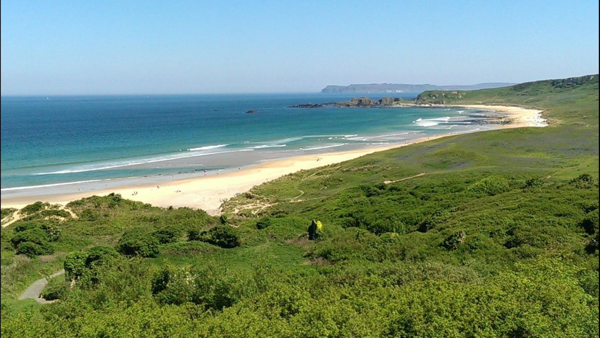 Un paisaje costero con playa, vegetación y una vista despejada del océano.