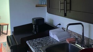 Una cucina con pensili scuri, un piano di lavoro in granito, una macchina da caffè e un lavandino con un portasciutto rosso.