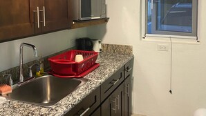 Una cucina con mobili scuri in legno, un lavello in acciaio inossidabile, un portascopini rosso e una finestra con persiane.