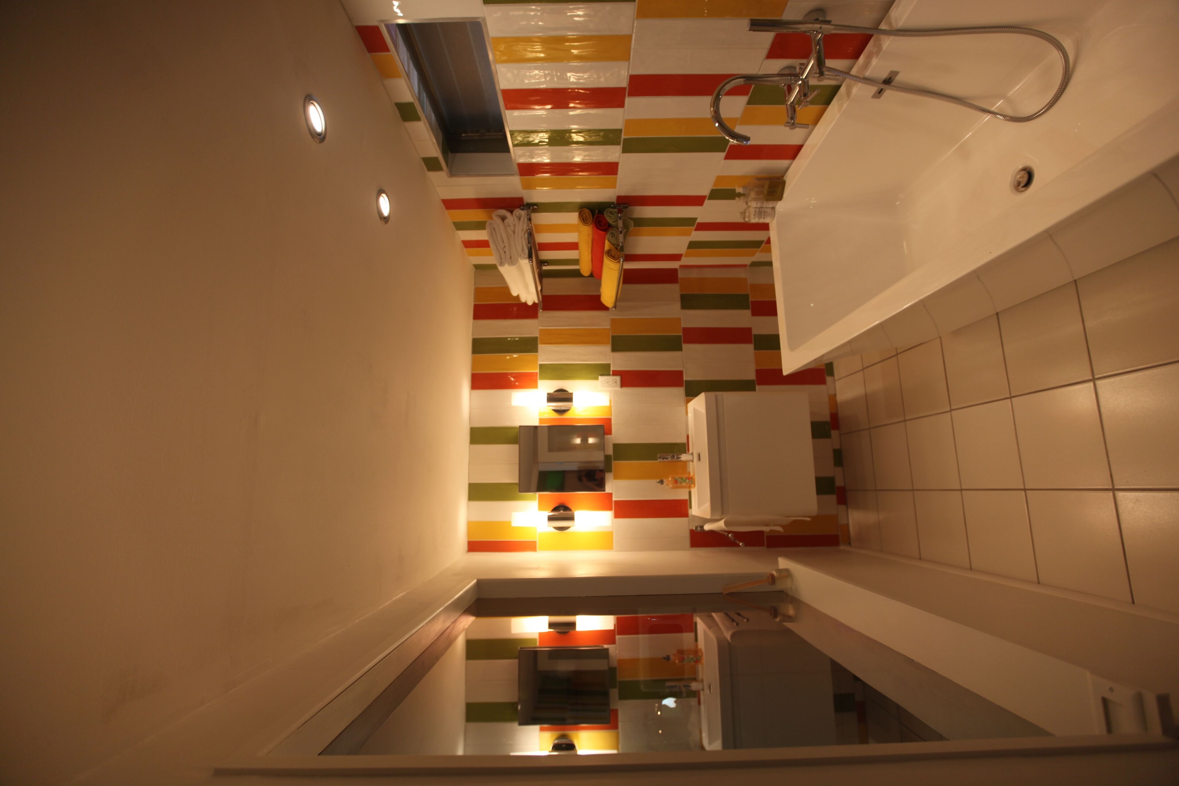 Une salle de bain moderne avec un mur décoré de rayures colorées, un espace douche et un lavabo avec un miroir.