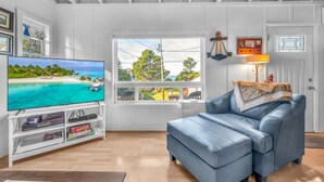 A living room with a TV, white walls, a window with a view of a beach, a blue sofa, and a lamp. - Pet-Friendly Cottage, Walk to Beach (Depoe Bay)