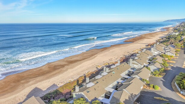 A coastal residential area with houses along the beach, clear skies, and ocean waves. - Pet-Friendly Cottage, Walk to Beach (Depoe Bay)