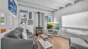 A modern living room with a fireplace, a television, and a bookshelf. - Pet-Friendly Cottage, Walk to Beach (Depoe Bay)