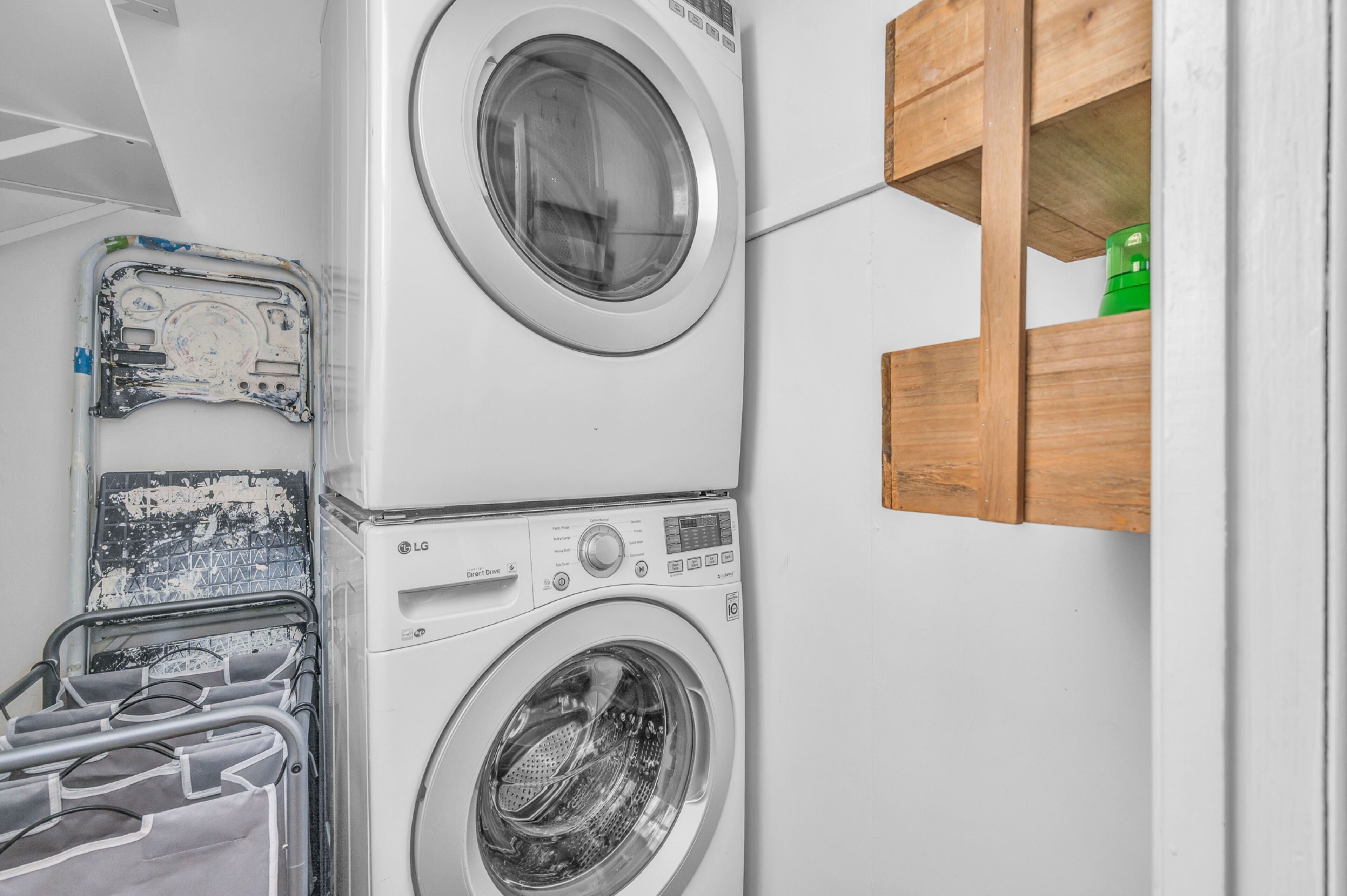 A stacked washer and dryer unit with a wooden shelf above it.